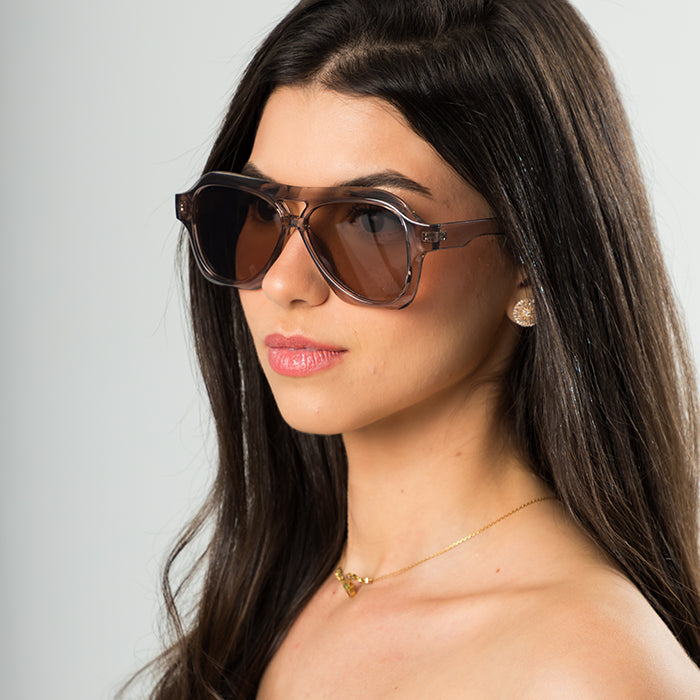Modelo utilizando óculos de sol feminino Rosa Coral Noasca, armação Marrom e lente Marrom – estilo sofisticado e proteção UVA e UVB 400 para os olhos.