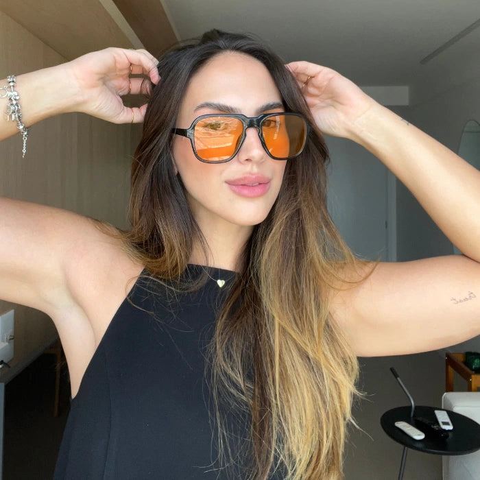 Modelo utilizando óculos de sol feminino Rosa Coral Messina, armação Preta e lente Laranja – estilo sofisticado e proteção UVA e UVB 400 para os olhos.