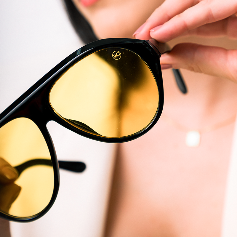 Modelo utilizando óculos de sol feminino Rosa Coral Norma, armação Preta e lente Amarela – estilo sofisticado e proteção UVA e UVB 400 para os olhos.