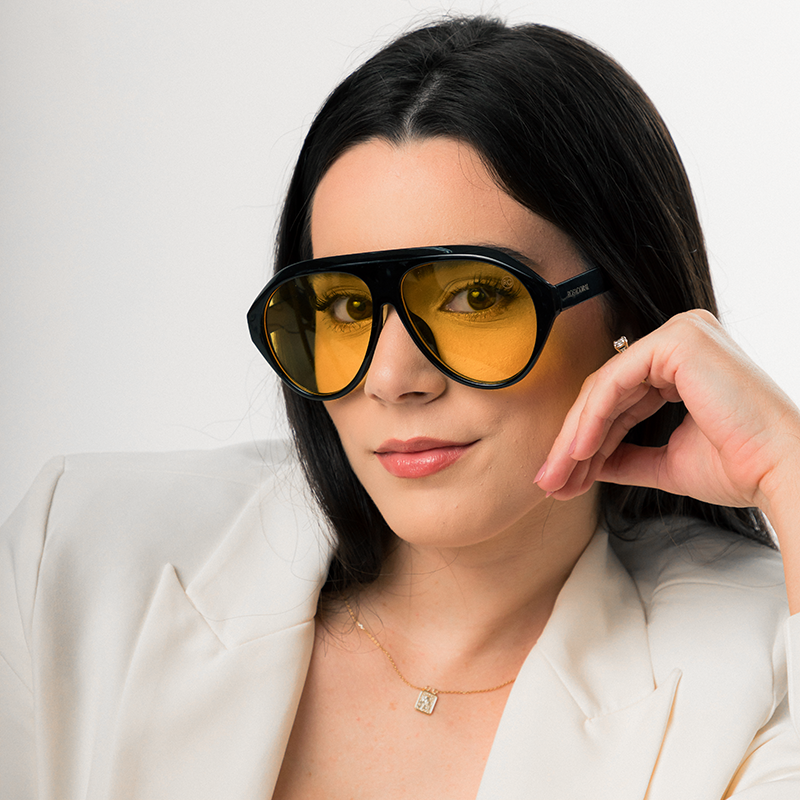 Modelo utilizando óculos de sol feminino Rosa Coral Norma, armação Preta e lente Amarela – estilo sofisticado e proteção UVA e UVB 400 para os olhos.