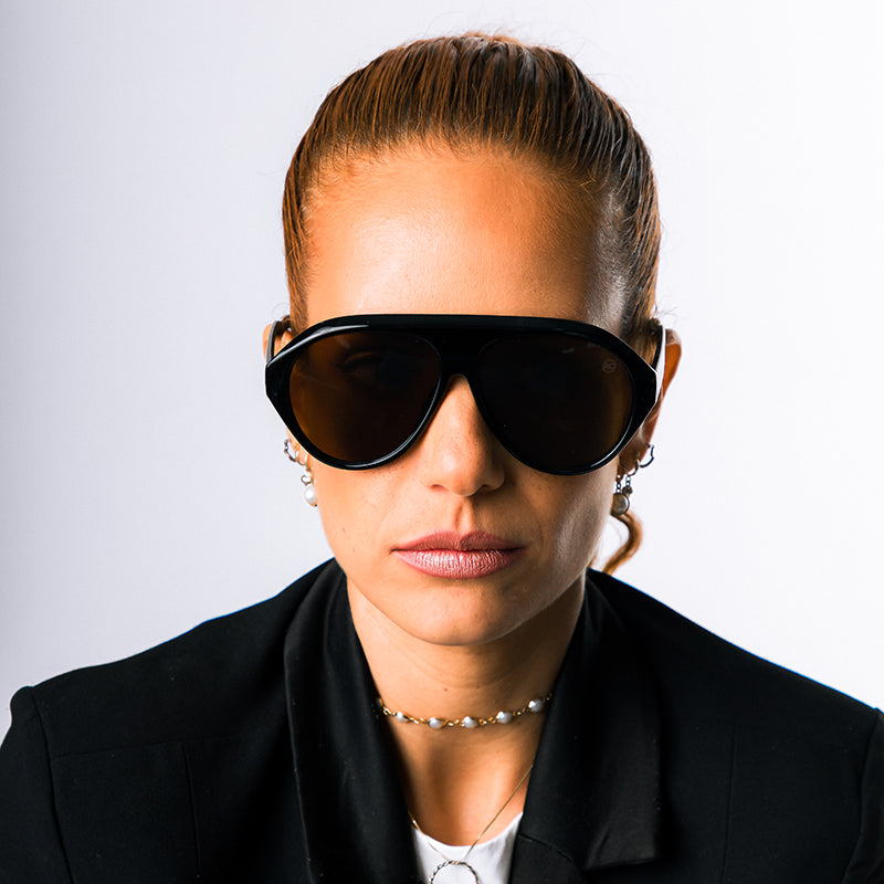 Modelo utilizando óculos de sol feminino Rosa Coral Norma, armação Preta e lente Marrom – estilo sofisticado e proteção UVA e UVB 400 para os olhos.