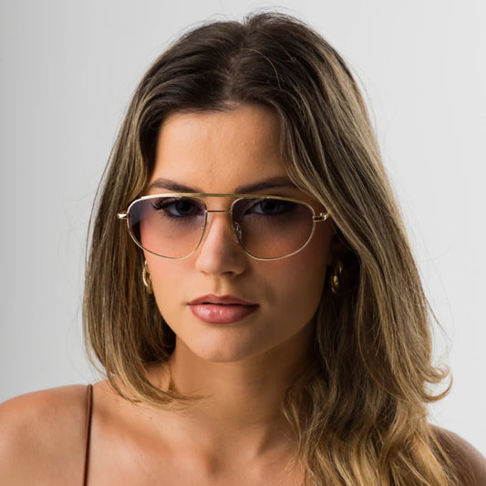 Modelo utilizando óculos de sol feminino Rosa Coral Aurelia, armação Dourado e lente Azul Gradiente – estilo sofisticado e proteção UVA e UVB 400 para os olhos.