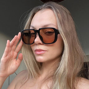 Modelo utilizando óculos de sol feminino Rosa Coral Castelli, armação Preta e lente Marrom – estilo sofisticado e proteção UVA e UVB 400 para os olhos.
