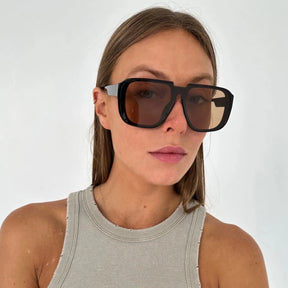 Modelo utilizando óculos de sol feminino Rosa Coral Castelli, armação Preta e lente Marrom – estilo sofisticado e proteção UVA e UVB 400 para os olhos.