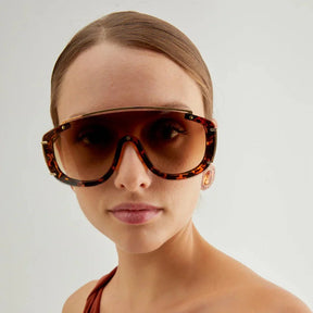 Modelo utilizando óculos de sol feminino aviador Rosa Coral Marsala, armação Leopardo e lente Marrom – estilo sofisticado e proteção UVA e UVB 400 para os olhos.