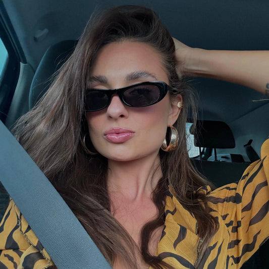 Modelo utilizando óculos de sol feminino Rosa Coral Matera, armação Preta e lente Preta – estilo sofisticado e proteção UVA e UVB 400 para os olhos.