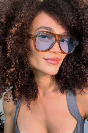 Modelo utilizando óculos de sol feminino Rosa Coral Noasca, armação Marrom e lente Azul – estilo sofisticado e proteção UVA e UVB 400 para os olhos.