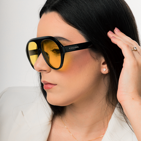 Modelo utilizando óculos de sol feminino Rosa Coral Norma, armação Preta e lente Amarela – estilo sofisticado e proteção UVA e UVB 400 para os olhos.