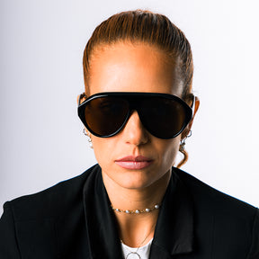 Modelo utilizando óculos de sol feminino Rosa Coral Norma, armação Preta e lente Marrom – estilo sofisticado e proteção UVA e UVB 400 para os olhos.