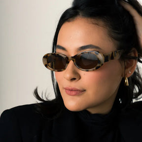 Modelo utilizando óculos de sol feminino Rosa Coral Ravena, armação Tartaruga e lente Marrom – estilo sofisticado e proteção UVA e UVB 400 para os olhos.