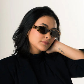 Modelo utilizando óculos de sol feminino Rosa Coral Ravena, armação Tartaruga e lente Marrom – estilo sofisticado e proteção UVA e UVB 400 para os olhos.