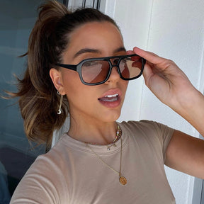 Modelo utilizando óculos de sol feminino Rosa Coral Roma, armação Preta e lente Marrom  – sofisticado e proteção UVA e UVB 400 para os olhos.