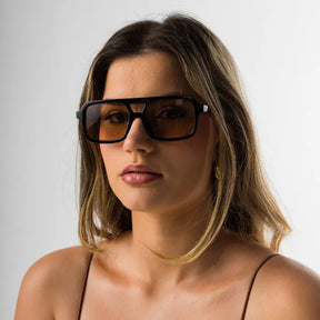 Modelo utilizando óculos de sol feminino Rosa Coral Roma, armação Preta e lente Marrom – sofisticado e proteção UVA e UVB 400 para os olhos.