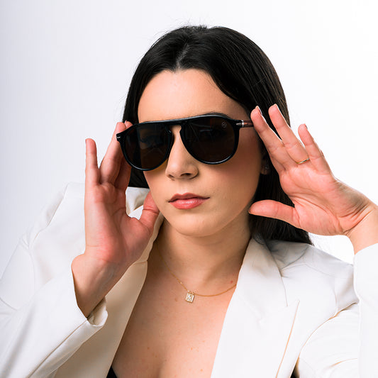Modelo utilizando óculos de sol feminino Rosa Coral Sassari, armação Preta e lente Marrom– estilo sofisticado e proteção UVA e UVB 400 para os olhos.