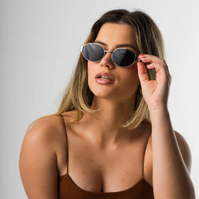 Modelo utilizando óculos de sol feminino Rosa Coral Selene, armação Dourada e lente Preta – estilo sofisticado e proteção UVA e UVB 400 para os olhos. 