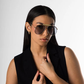 Modelo utilizando óculos de sol feminino Rosa Coral Sicilia, armação Dourada e lente Cinza – estilo sofisticado e proteção UVA e UVB 400 para os olhos.