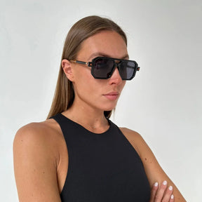 Modelo utilizando óculos de sol feminino aviador Rosa Coral Villanova, armação Preta e lente Cinza – estilo sofisticado e proteção UVA e UVB 400 para os olhos.