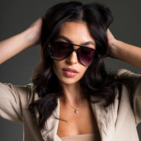 Modelo utilizando óculos de sol feminino Rosa Coral Marche, armação Preta e lente Roxo Degradê – estilo sofisticado e proteção UVA e UVB 400 para os olhos.